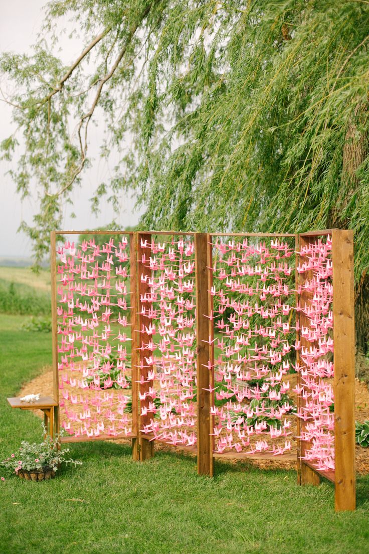 pink paper flowers are placed on the side of a wooden fence in front of a tree