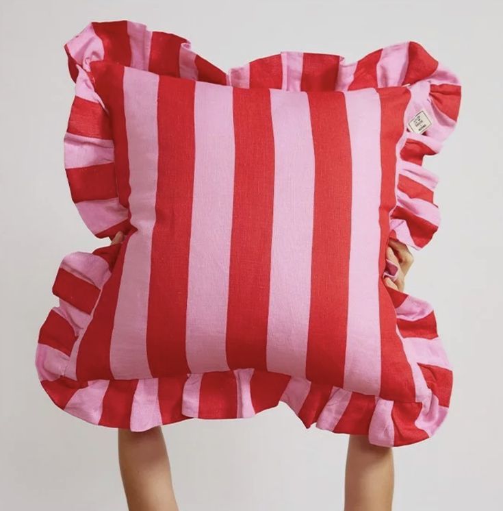 a pink and red striped pillow with ruffles on the bottom, in front of a white wall