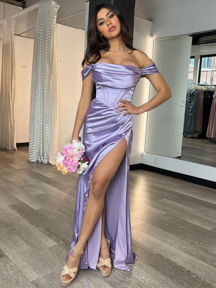 A woman is posing in a stylish, lavender, off-shoulder gown with a thigh-high slit, holding a bouquet of flowers, in a well-lit boutique with mirrors and draped fabrics. Lavender Satin Dress, Lavender Gown, Bachelorette Party Dress, Champagne Dress, Rehearsal Dinner Dresses, Corset Bodice, Rehearsal Dress, Custom Size Dresses, Ladies Gown