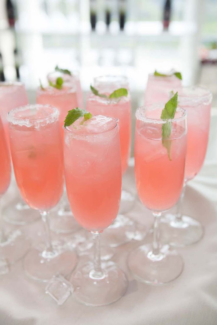 several glasses filled with pink liquid and garnished with mint leaves on a white table cloth