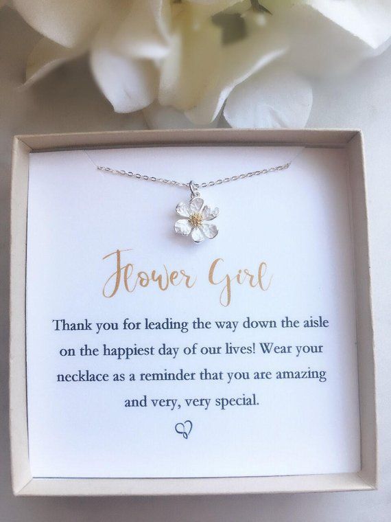 a flower girl necklace in a gift box next to a white carnation and some flowers