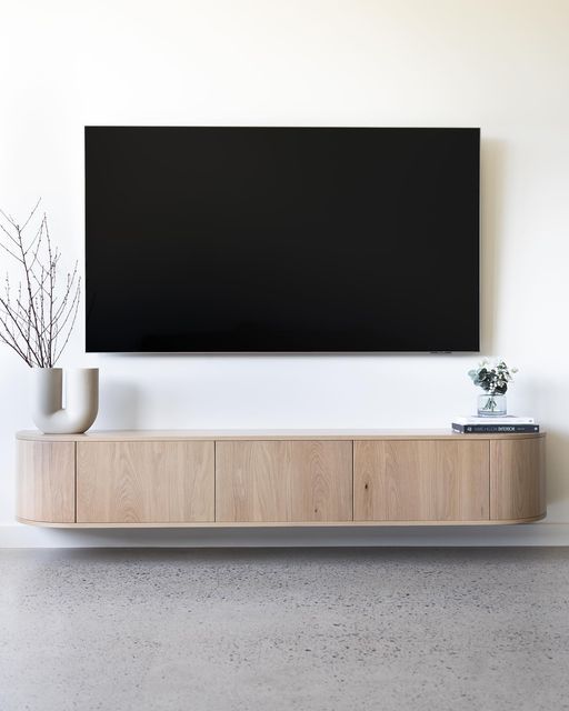 a large flat screen tv mounted on the wall above a wooden cabinet with vases