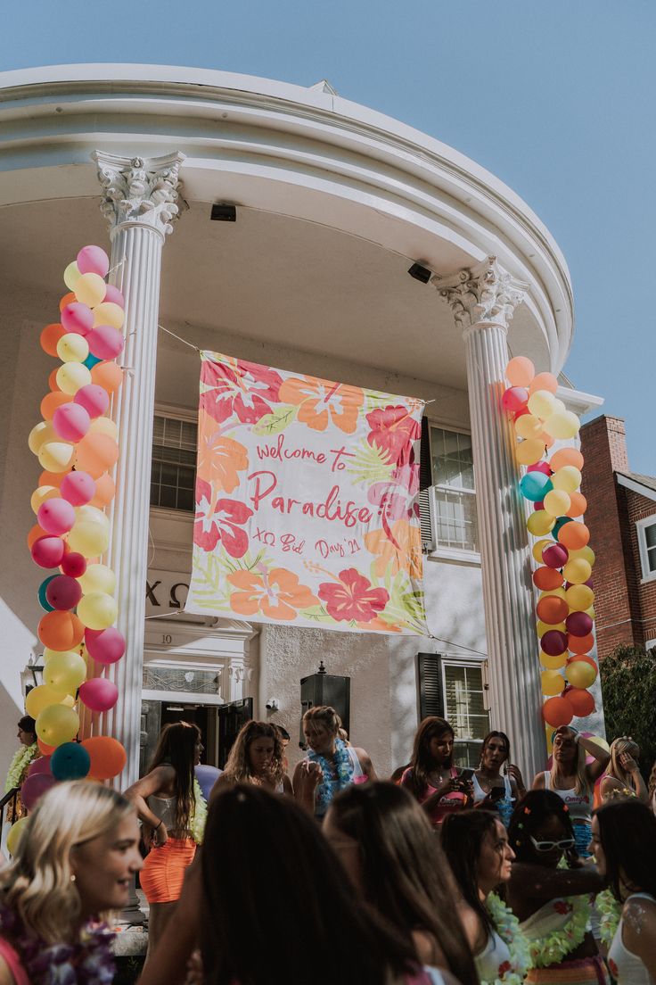 a large group of people standing in front of a building with balloons on the ground