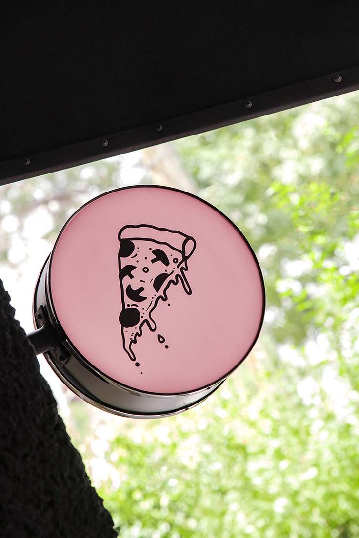 a pink and black sign with a slice of pizza on it's side hanging off the side of a tree