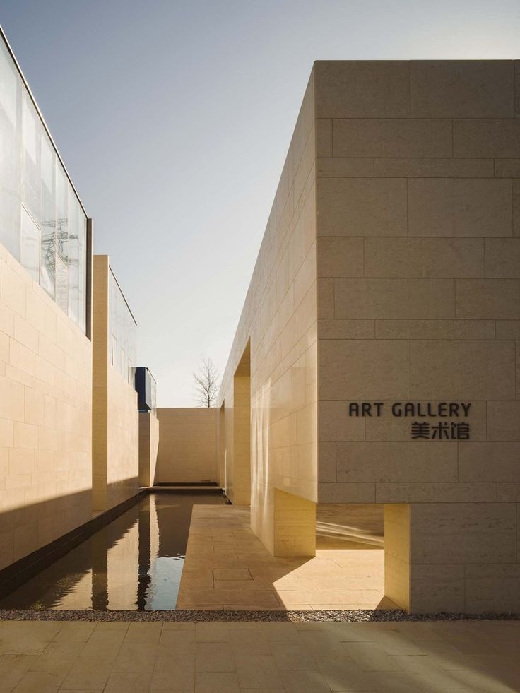 an art gallery building with water in the foreground and sun shining on the wall