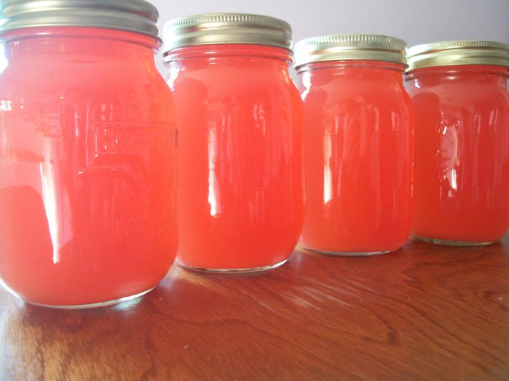 four mason jars lined up on a table with one filled with watermelon liquid