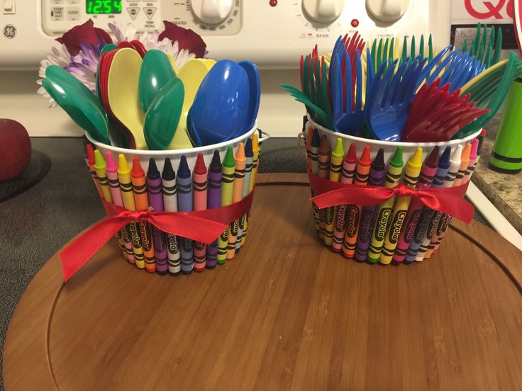 two cups filled with colorful crayons and spoons on top of a table