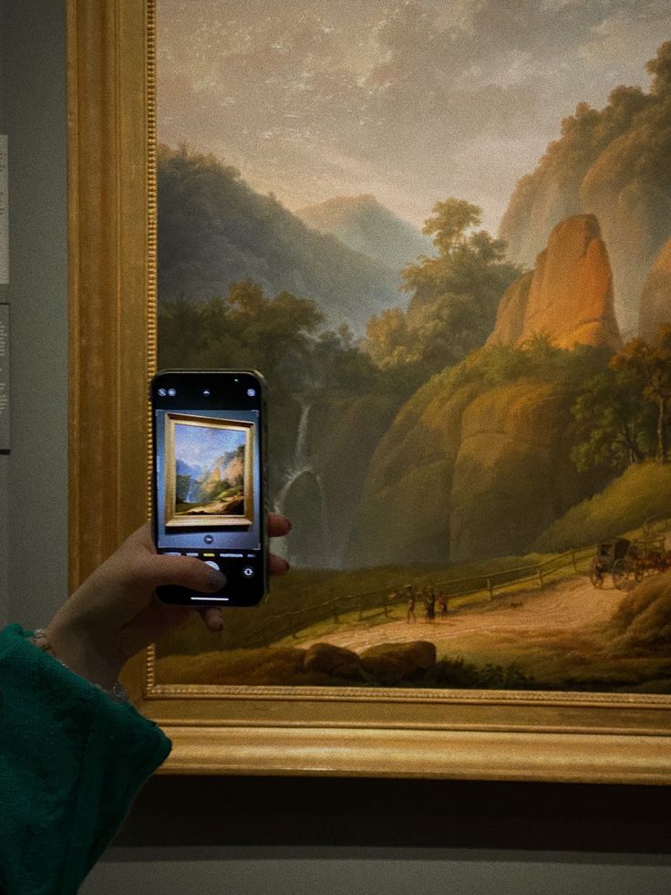 a person holding up a cell phone in front of a painting