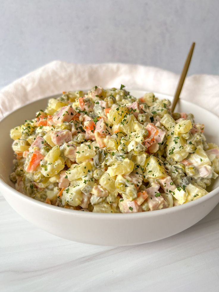 a white bowl filled with potato salad on top of a table next to a wooden spoon