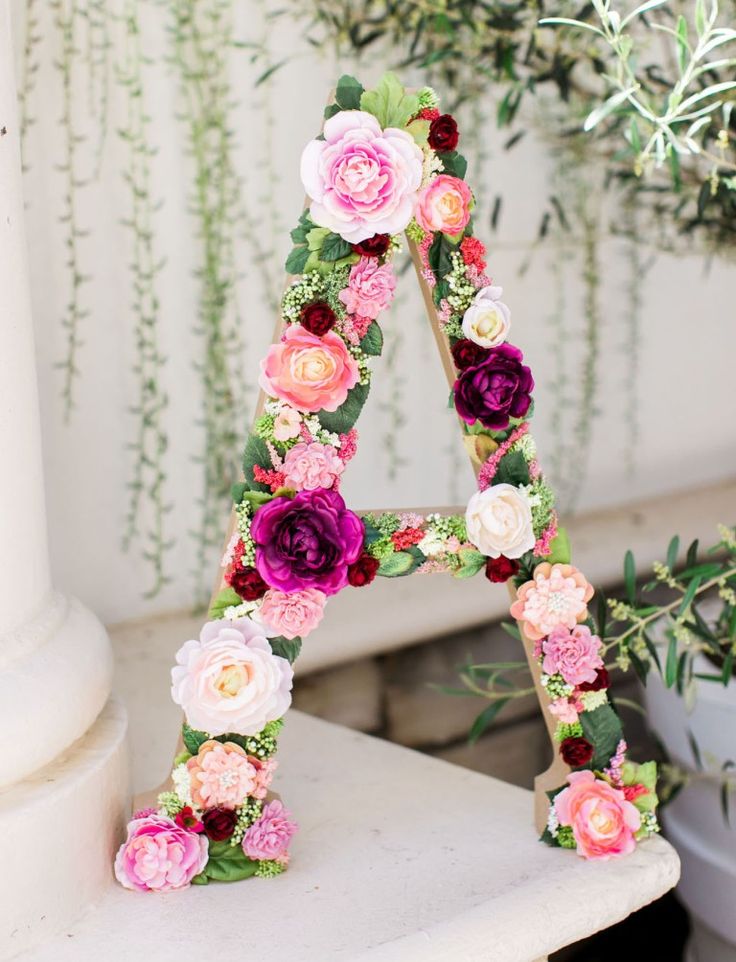 a floral letter sitting on top of a white table next to a potted plant