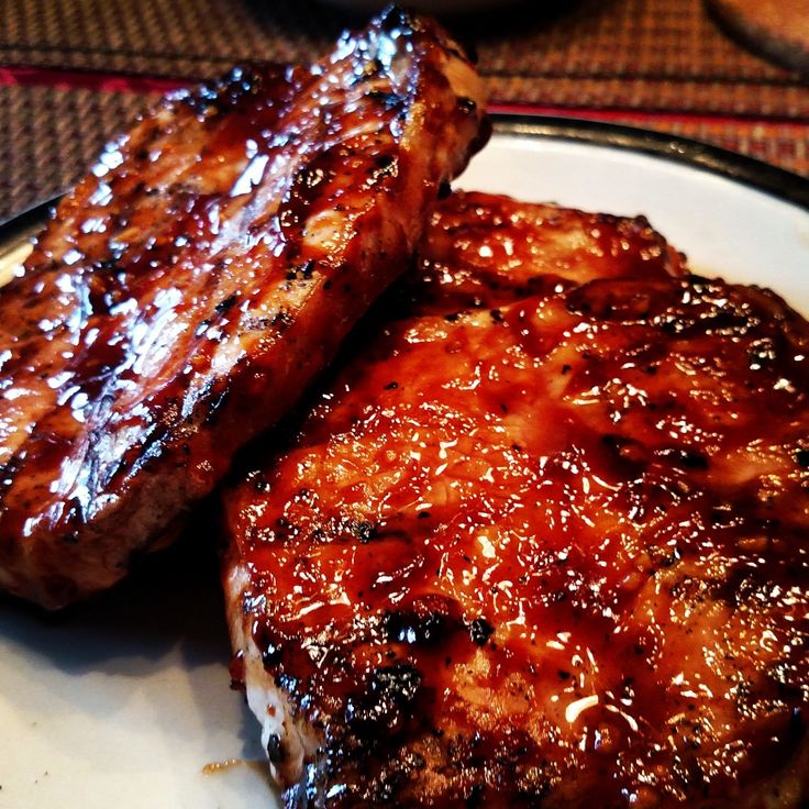 two pieces of meat sitting on top of a white plate covered in bbq sauce