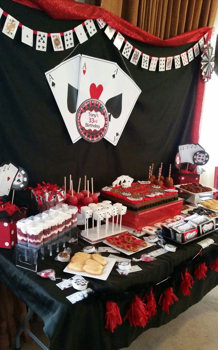 a table topped with lots of cakes and desserts next to a casino themed wall