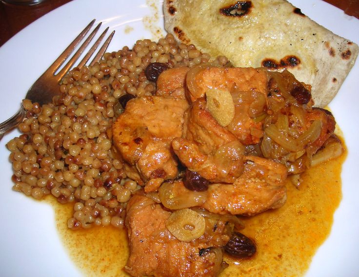 a white plate topped with meat and beans next to a piece of pita bread