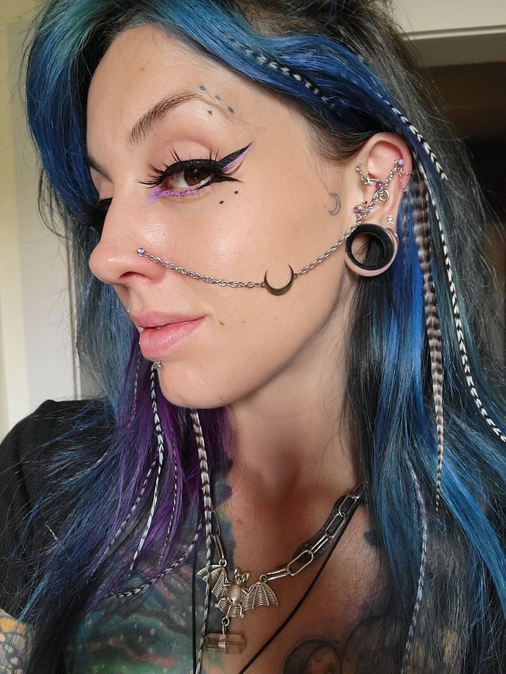 a woman with blue hair has piercings on her face and is wearing ear rings