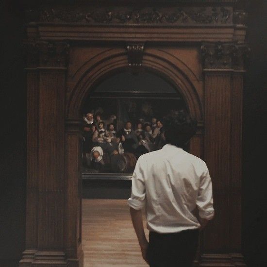 a man in white shirt and black pants looking at painting