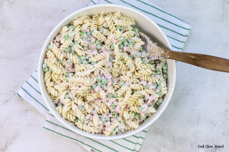 a white bowl filled with pasta and peas on top of a green striped towel next to a wooden spoon