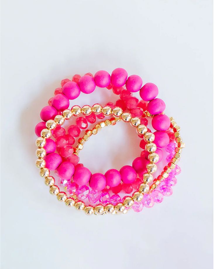 three pink and gold beaded bracelets on a white surface, with one being held in the other's hand