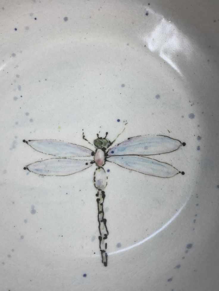 a dragonfly sitting on top of a white plate with blue speckles around it