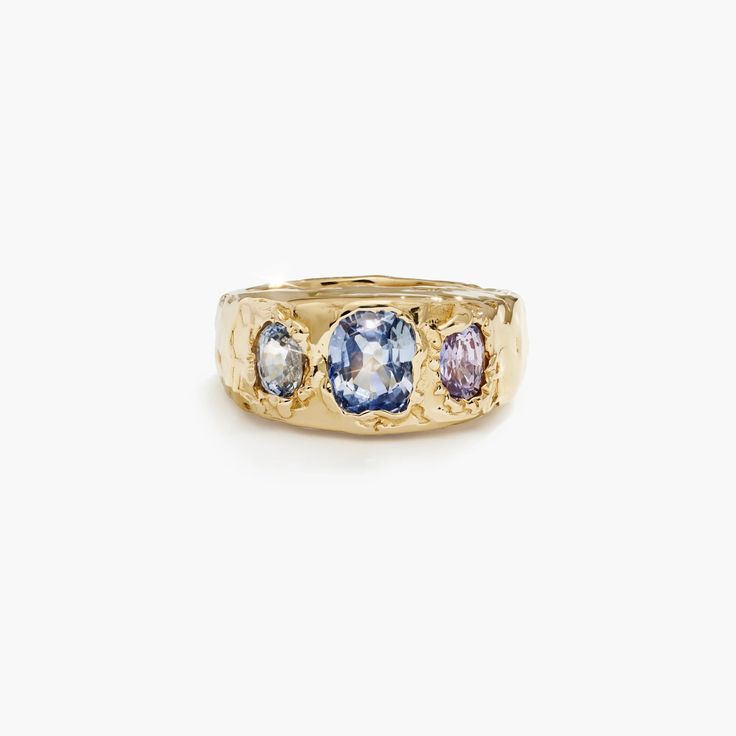 three stone ring in yellow gold with blue and white stones on the sides, set against a white background