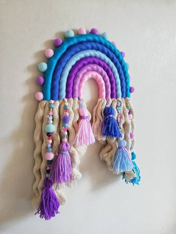 a rainbow wall hanging with tassels and pom poms on the sides