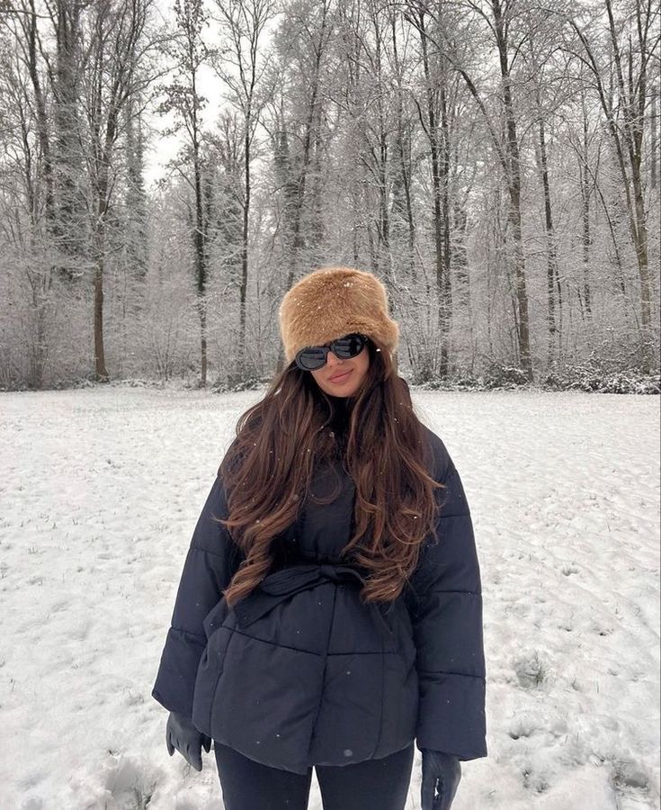 a woman standing in the snow with her hands on her hips wearing sunglasses and a fur hat