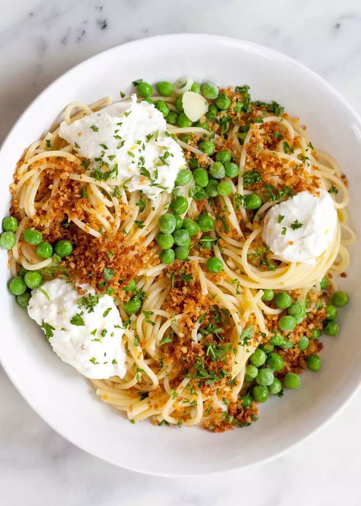 a white bowl filled with pasta, peas and parmesan on top of a marble table