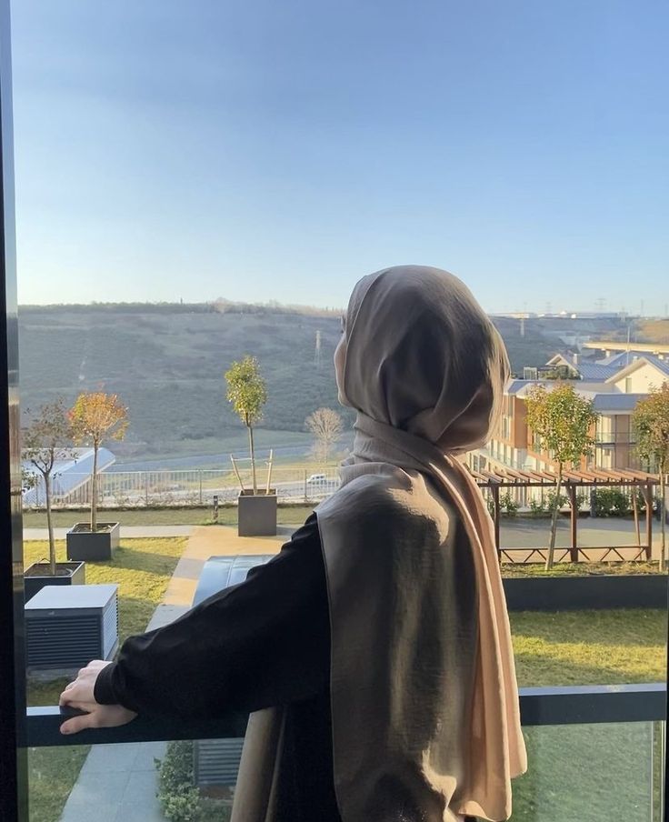 a woman standing in front of a window looking out at a cityscape and hills