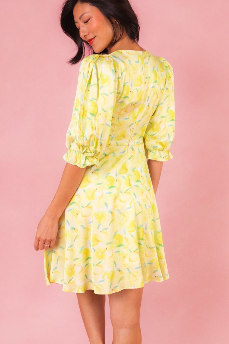 Introducing the Lita Dress, your sunny day delight straight from the orchard! Made from vibrant yellow, green, and white fruit-print satin fabric, this dress features a charming round neckline and 3/4 length puff sleeves with elastic closure, adding a playful touch to your summer wardrobe. With a knee-length skirt adorned with pockets and a hidden back zipper for easy wear, it's the perfect blend of style and practicality for picnics, brunches, and everything in between. Spring Garden Party Dress With Fruit Print, Green Fruit Print Dresses For Spring, Spring Brunch Dress With Fruit Print, Yellow Half Sleeve Dress For Spring, Yellow Half Sleeve Spring Dress, Yellow Summer Dress With Fruit Print, Fruit Print Short Sleeve Dresses For Brunch, Short Sleeve Fruit Print Dress For Brunch, Short Sleeve Brunch Dress With Fruit Print