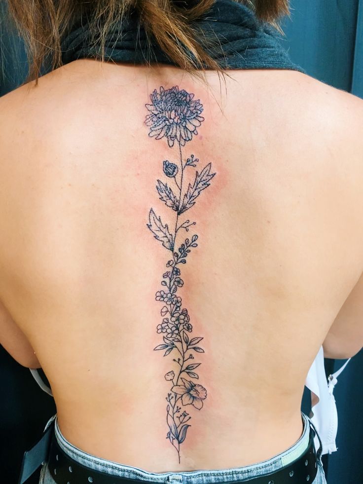 the back of a woman's upper back tattoo with flowers and leaves on it