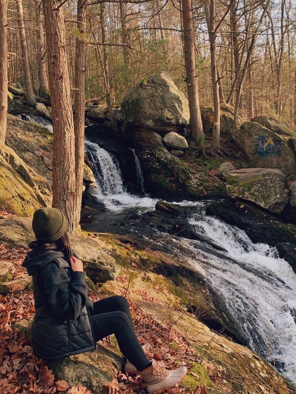 a woman sitting on the ground next to a waterfall