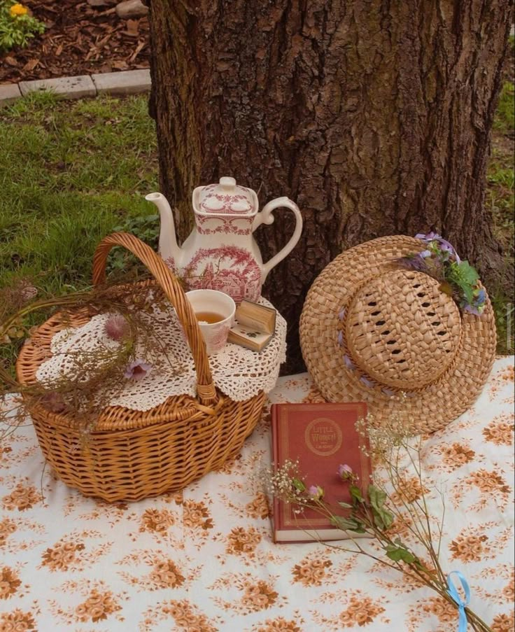 tea and books on a table next to a tree in the grass near a basket