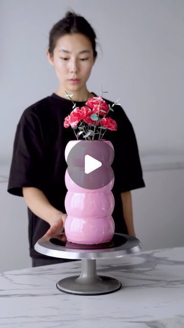 a woman standing in front of a cake with red flowers on it and a video playing