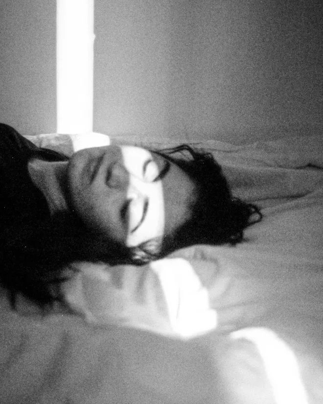 a black and white photo of a woman laying on a bed with her eyes closed