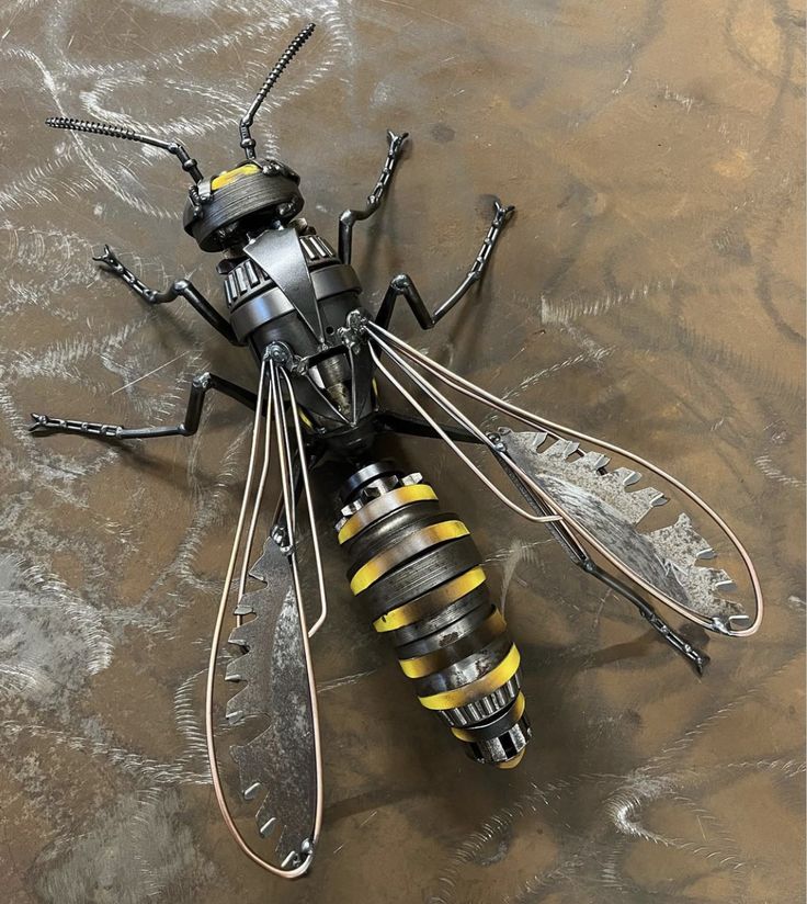 a metal sculpture of a bee with yellow stripes on it's body and wings