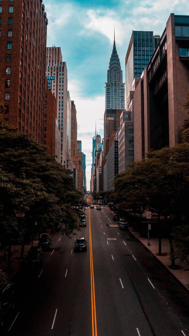 an empty city street with tall buildings in the back ground and cars on the road