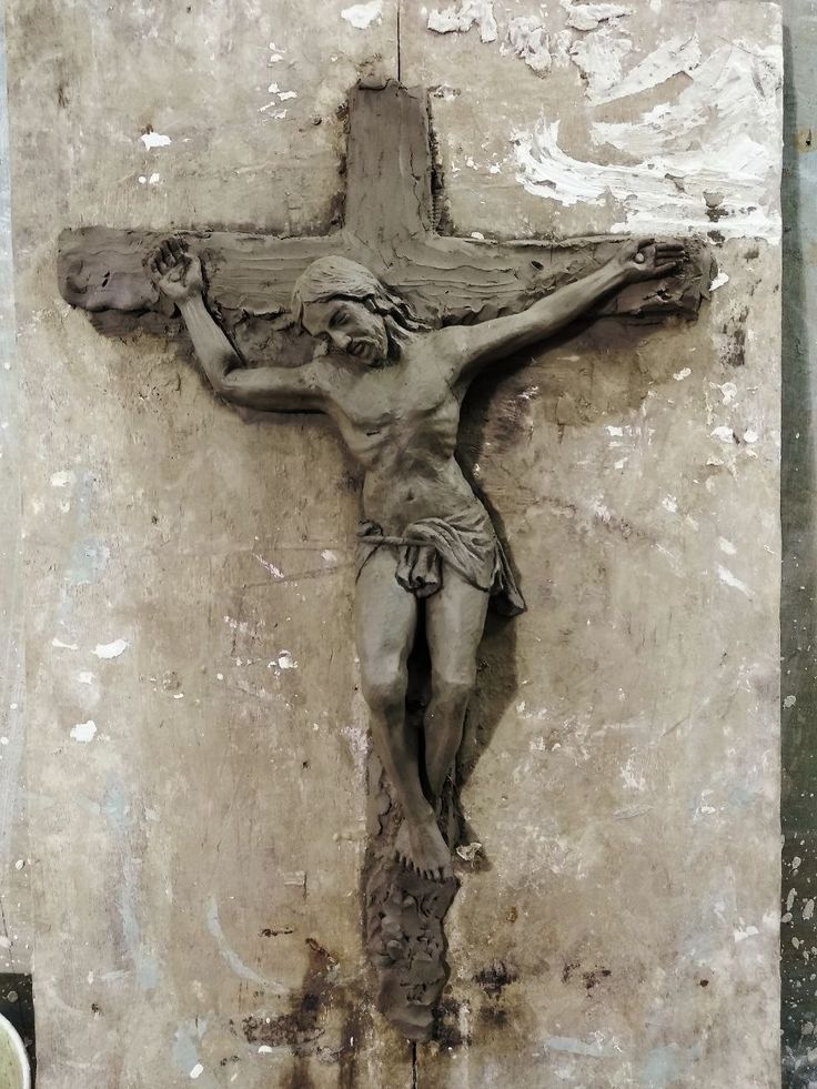 a statue of jesus on the cross in front of a wall with paint peeling off it