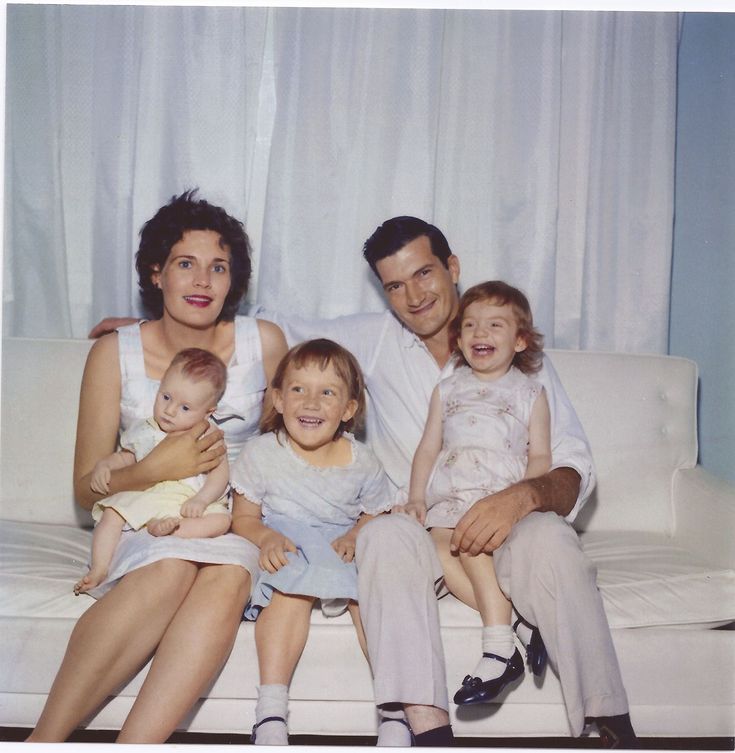 a family sitting on a white couch posing for a photo with their two children and one adult