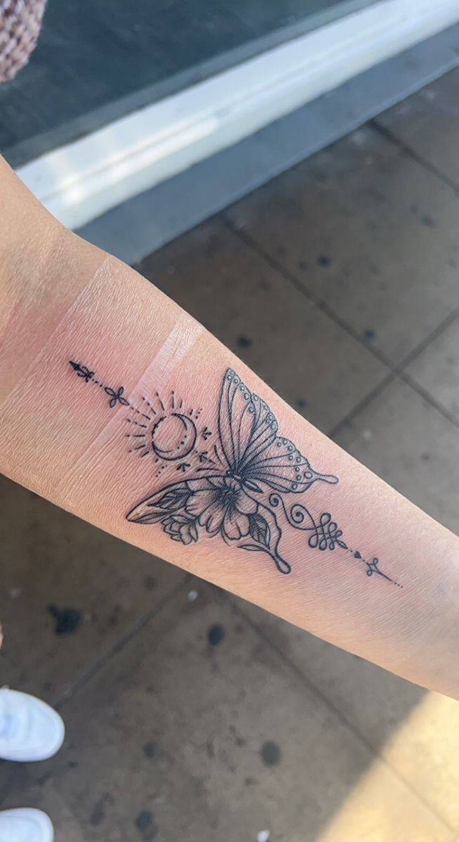 a small butterfly tattoo on the left forearm and right arm, with stars in the background