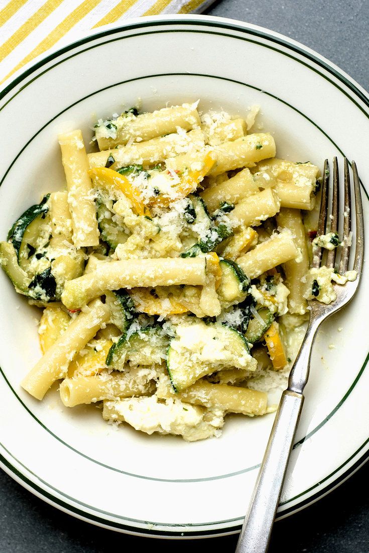 a white plate topped with pasta and spinach next to a yellow striped napkin on top of a table