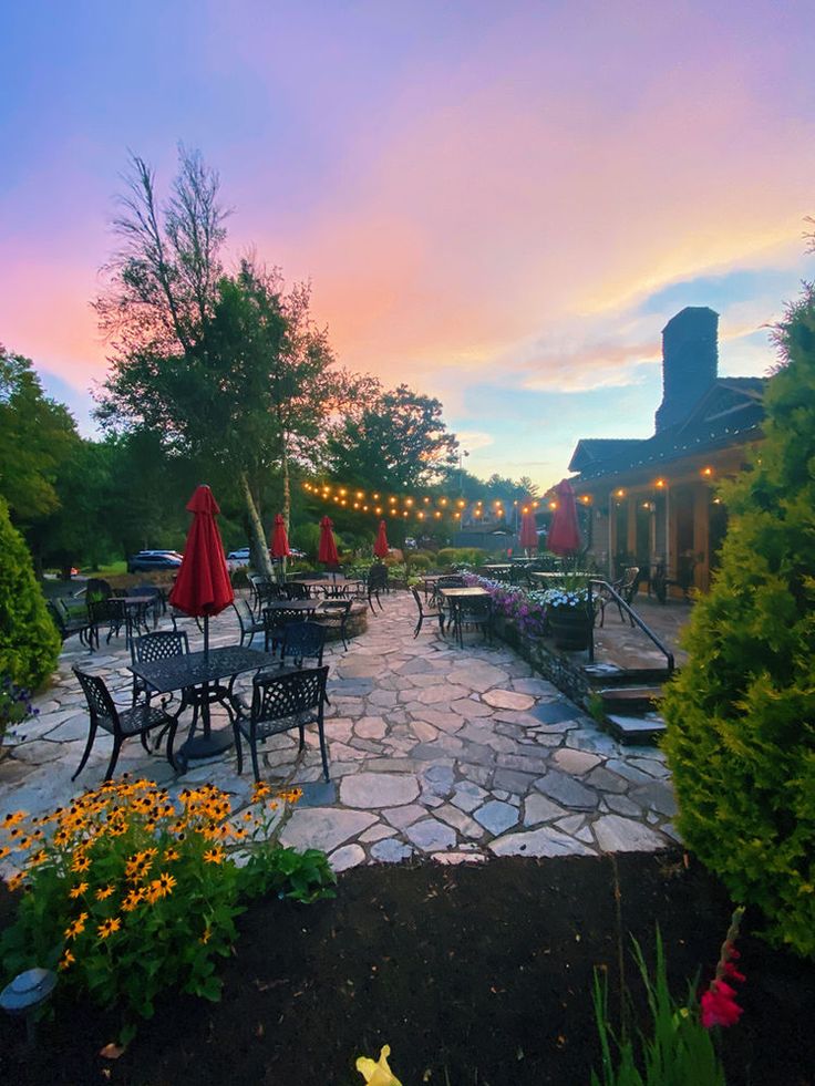 an outdoor patio with tables and umbrellas at sunset or dawn, surrounded by greenery