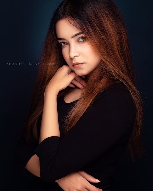 a woman with long brown hair posing for a photo in front of a dark background