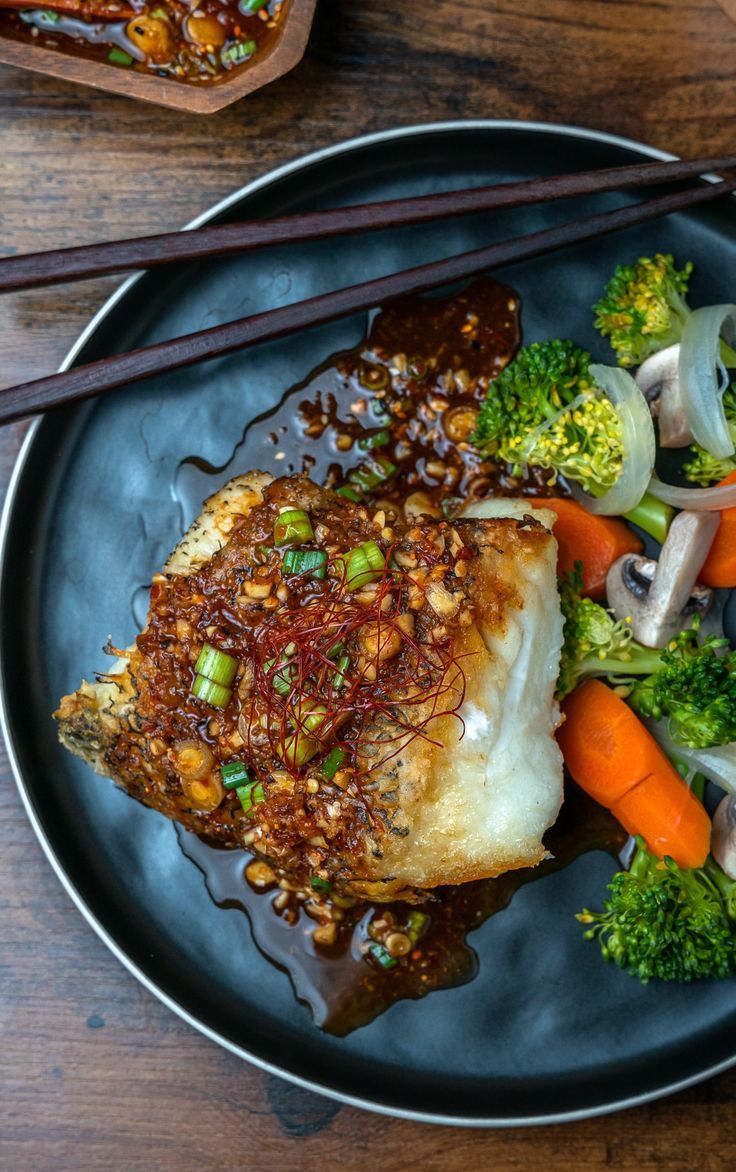 a black plate topped with fish and vegetables