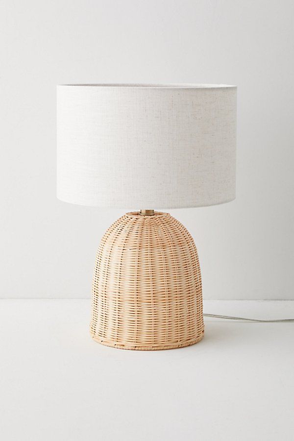 a wicker table lamp with a white shade on the base and a light bulb attached to it