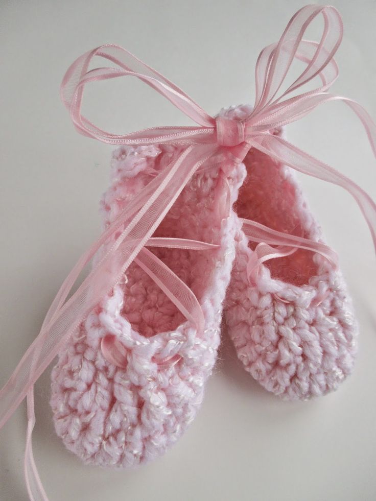 a pair of pink crocheted baby shoes tied up to a white table top