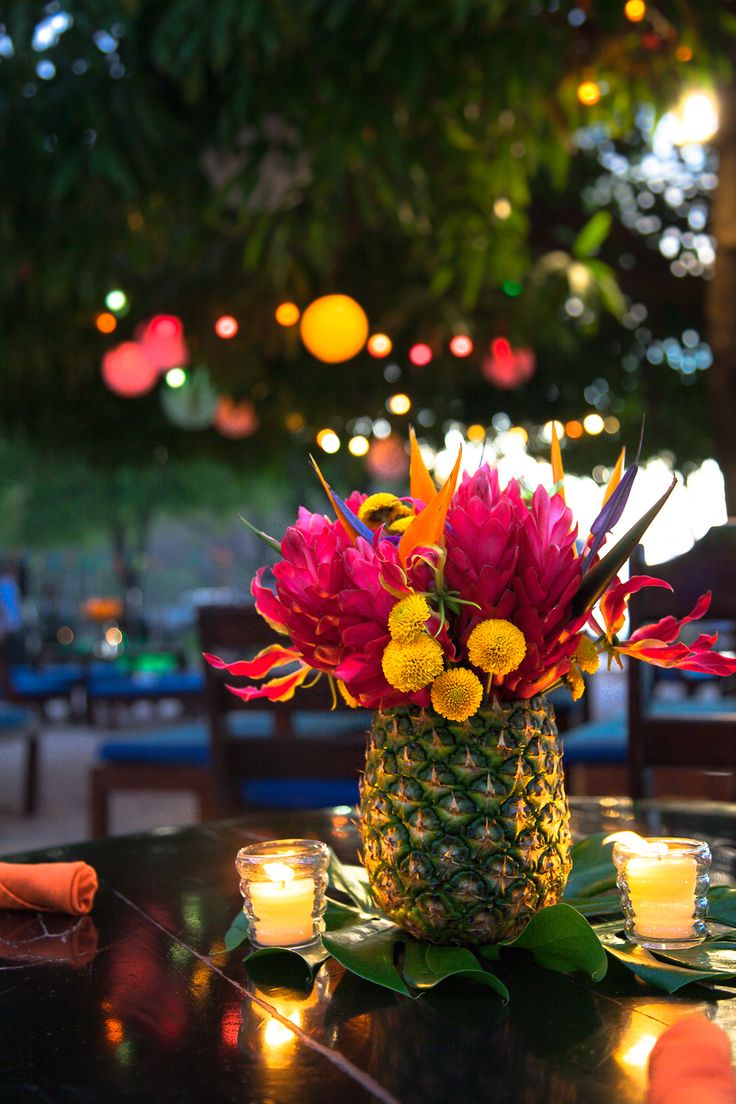 a pineapple vase filled with flowers on top of a table next to lit candles