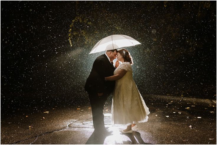 a bride and groom kissing under an umbrella in the rain at their wedding reception on a rainy night