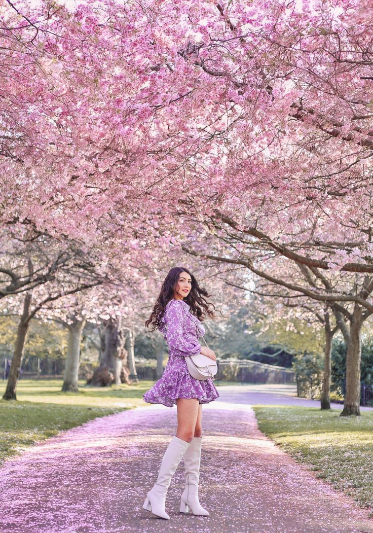 a woman in a purple dress and white boots standing under cherry blossom trees