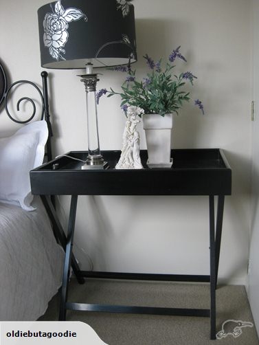 a small black table with a lamp on it next to a bed