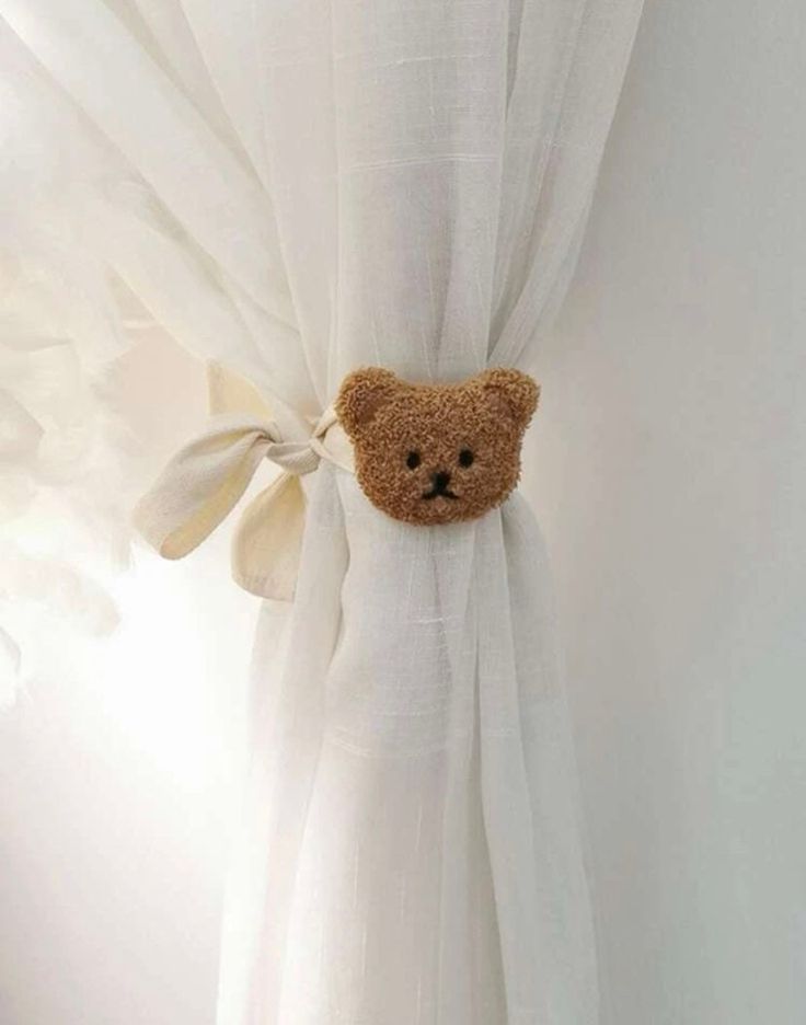 a teddy bear peeking out from behind a white curtain with a bow on it's head