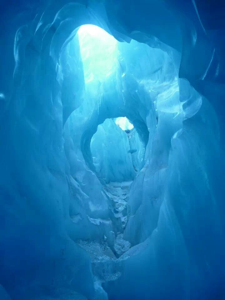 the inside of an ice cave with light coming from it's opening and blue water